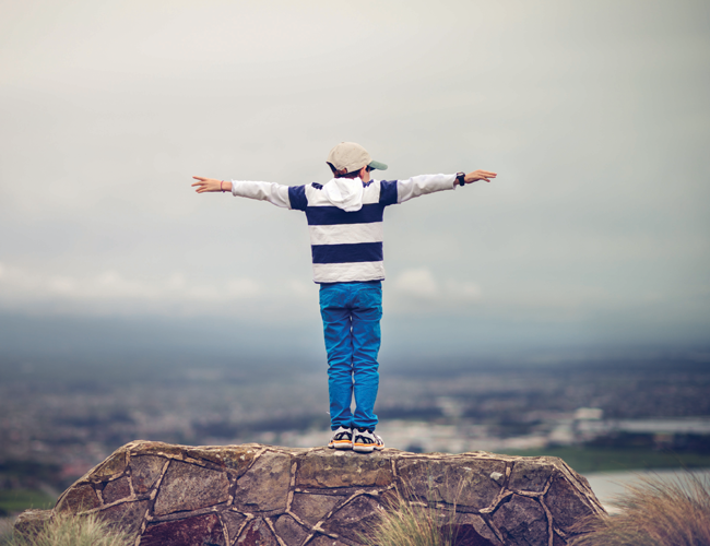 Boy standing on rock with arms out stretched